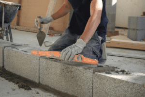 Maçon d'une entreprise de maçonnerie, en train de poser des blocs de béton et de vérifier le niveau avec un outil à bulle, illustrant les travaux de maçonnerie sur un chantier de construction.