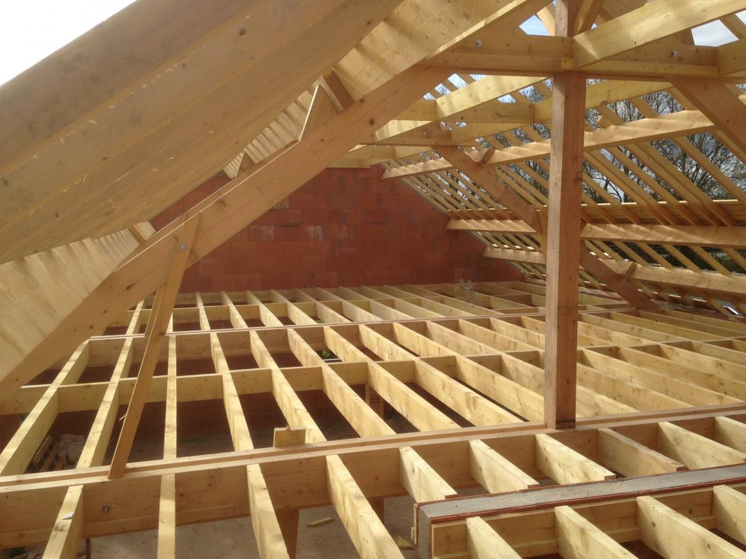 Charpente en bois d'un toit en construction par une entreprise de charpenterie professionnelle, avec des poutres visibles, représentant la structure d'une maison en cours de construction.